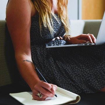 person sitting on a couch and making notes while watching a webinar on business 